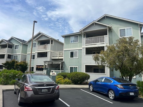Two cars parked in a parking lot in front of apartment buildings.