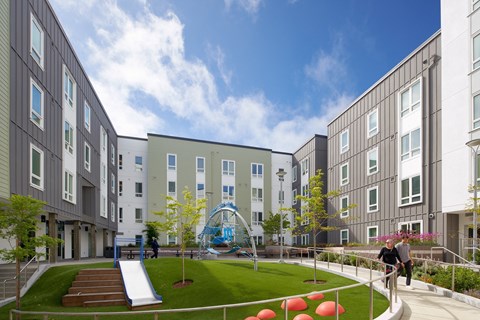 A playground area with a slide and a green lawn in the middle of a courtyard surrounded by buildings.