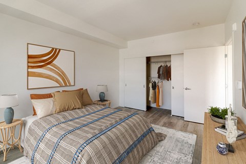 A bedroom with a bed, a lamp, a painting, a wardrobe and a plant.