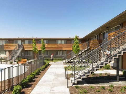 A man is walking down a path in front of a building with a pool.