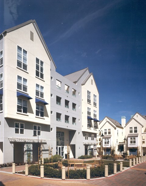 A row of white buildings with balconies and a red brick walkway in front.