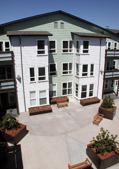 A courtyard with a bench and a planter in front of a white building.