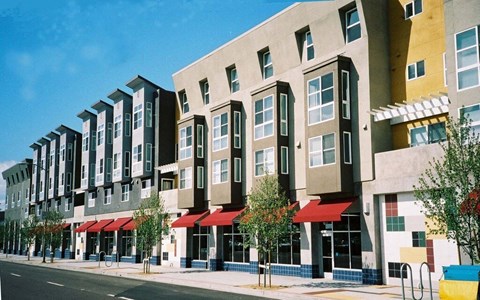 A row of modern apartment buildings with red awnings line a street.