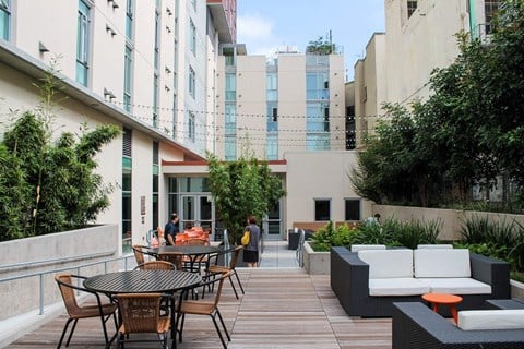 A patio with a table and chairs is surrounded by buildings and greenery.