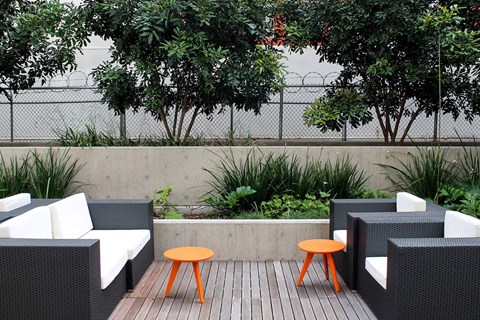 A patio with a black wicker sofa, a small orange table, and a white cushion.