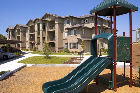 A playground with a green slide in front of apartment buildings.