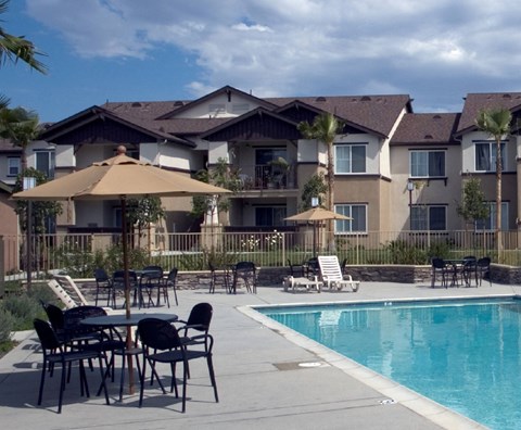 A pool area with chairs and umbrellas in front of apartment buildings.