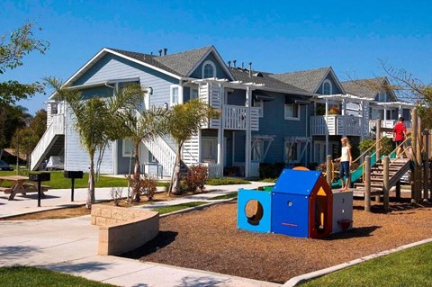 A playground with a slide and a playhouse in front of a row of houses.