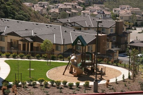 A playground with a slide and swings in the foreground and houses in the background.