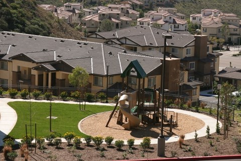 A playground with a slide and a green roofed building in the background.