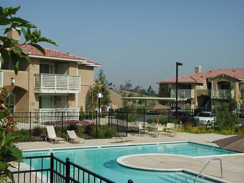 A pool in a fenced in area with chairs around it.