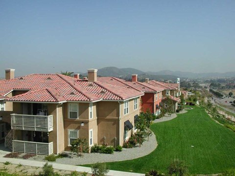 A row of houses with red roofs and green lawns.