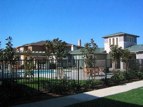 A pool is surrounded by a black fence and green trees.