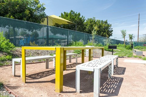 A playground with a yellow and grey slide and a green fence.