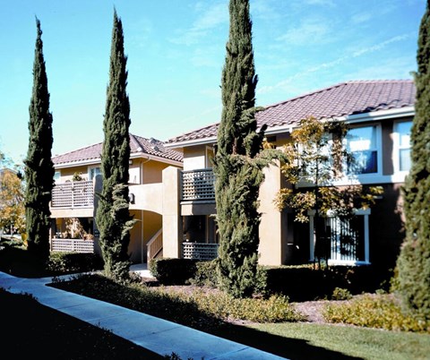 A house with a red roof and a balcony is surrounded by tall trees.