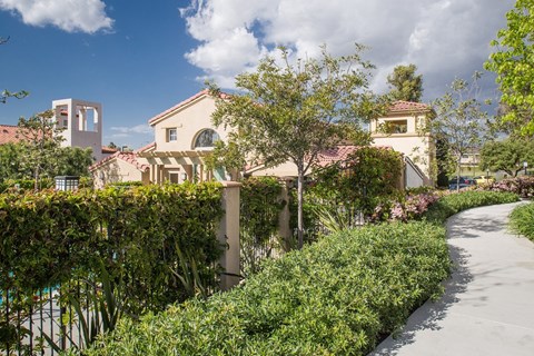 A pathway leads through a lush garden with a building in the background.