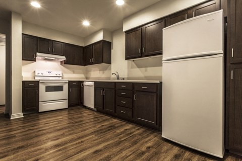 A white refrigerator stands in a kitchen with dark wood cabinets.