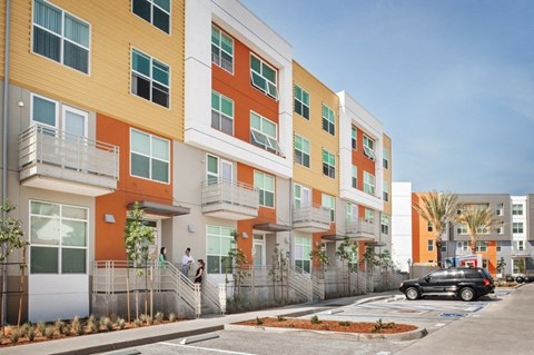 A row of modern apartment buildings with balconies and trees in front.