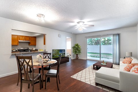 A living room with a couch, a dining table with chairs, and a kitchen area with a countertop and cabinets.