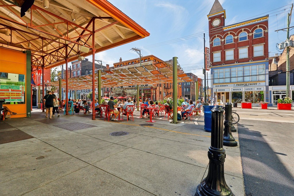 People enjoying outdoor dining at Findlay Market in Over-the-Rhine Cincinnati with red patio seating and lively atmosphere.