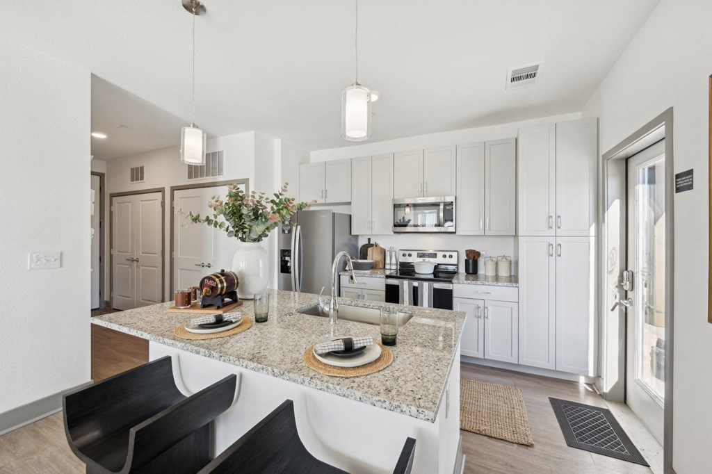 A modern kitchen with a granite countertop and black chairs.