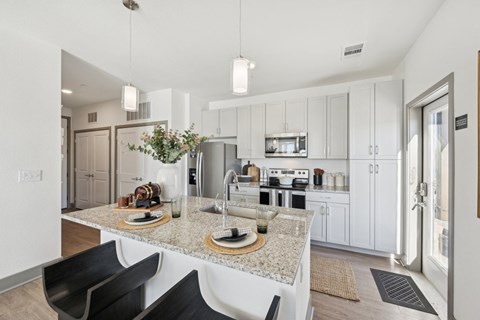 A modern kitchen with a granite countertop and black chairs.
