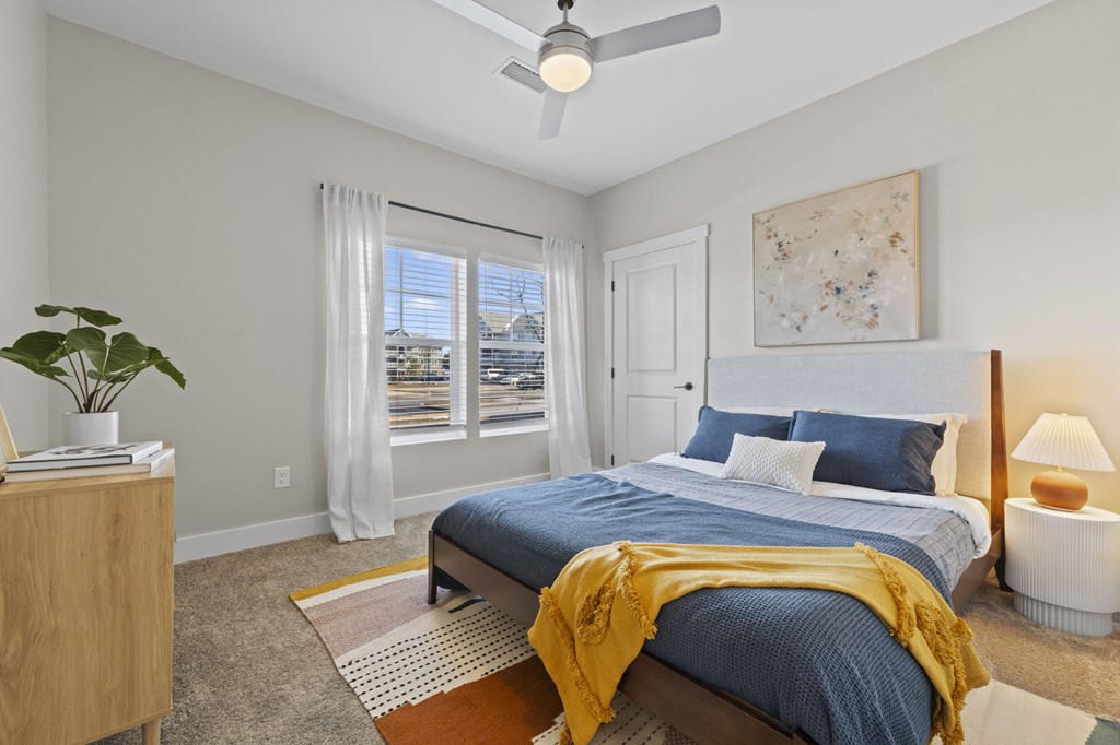 A bedroom with a bed, a ceiling fan, and a window with a view of buildings outside.