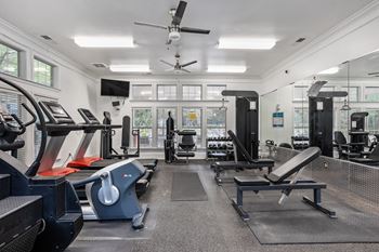 A spacious gym with a variety of equipment including treadmills, weight machines, and a ceiling fan.