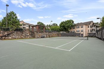 A tennis court with a stone wall and a building in the background.