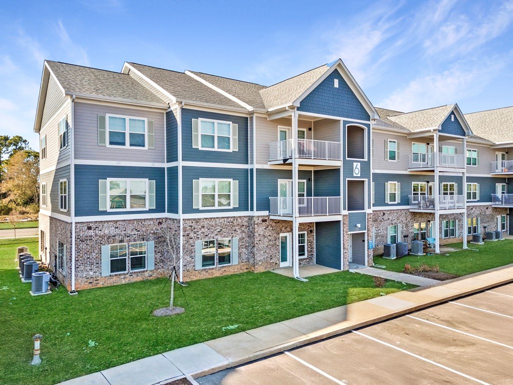 A large apartment complex with multiple balconies and a parking lot in front.