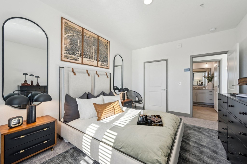 A bedroom with a bed, nightstand, and a large mirror.