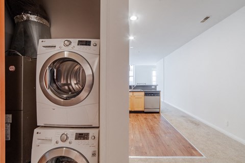 a washer and dryer in a laundry room with a kitchen in the background at 26 West, Managed by Buckingham Urban Living, Indianapolis