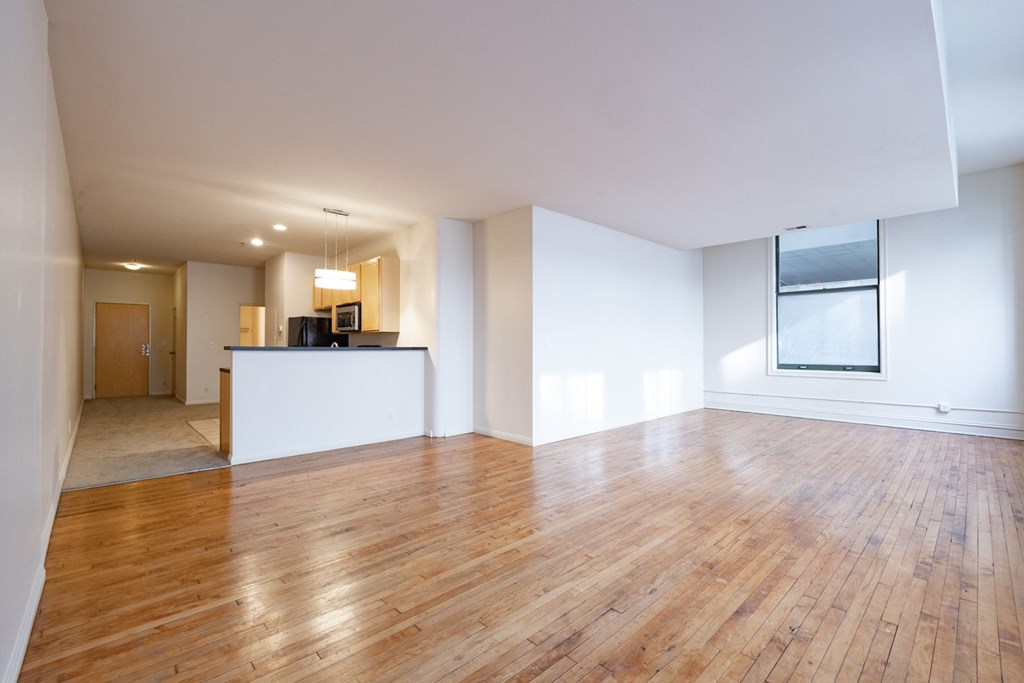 an empty living room with hardwood floors and a kitchen in the background at 26 West, Managed by Buckingham Urban Living, Indianapolis