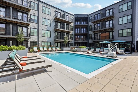 A swimming pool surrounded by lounge chairs and apartment buildings.
