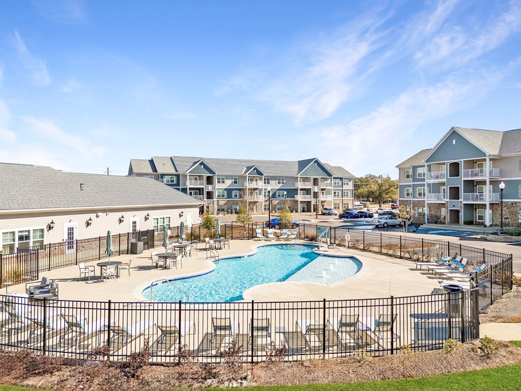 A large outdoor pool surrounded by a black fence and lounge chairs.