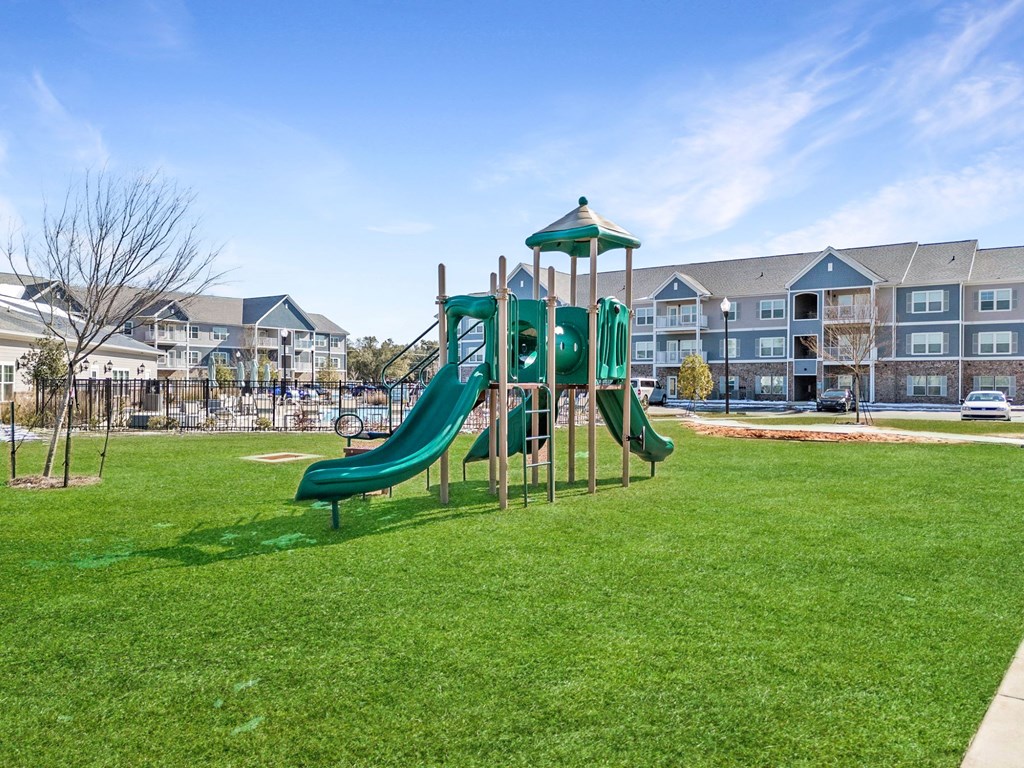 A green slide in a playground with apartment buildings in the background.