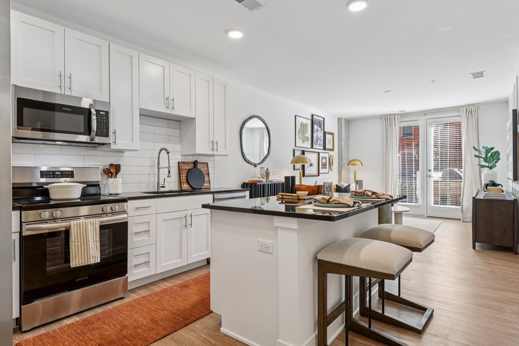 Modern kitchen at Contrast OTR in Cincinnati, OH featuring stainless steel appliances, white cabinetry, and a breakfast island with seating.