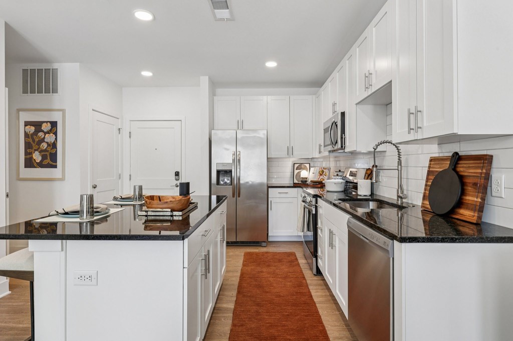 Sleek kitchen at Contrast OTR apartments in Cincinnati, OH with a large center island, modern lighting, and white shaker cabinets.