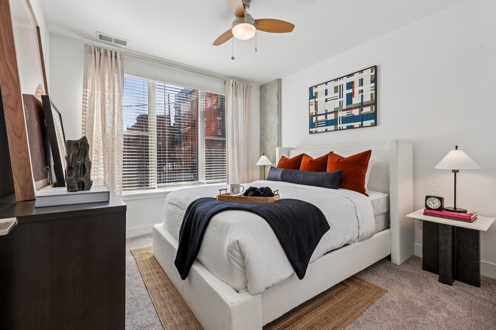 Bedroom interior at Contrast OTR apartments in Cincinnati, OH featuring bold accent pillows, urban views, and natural light.