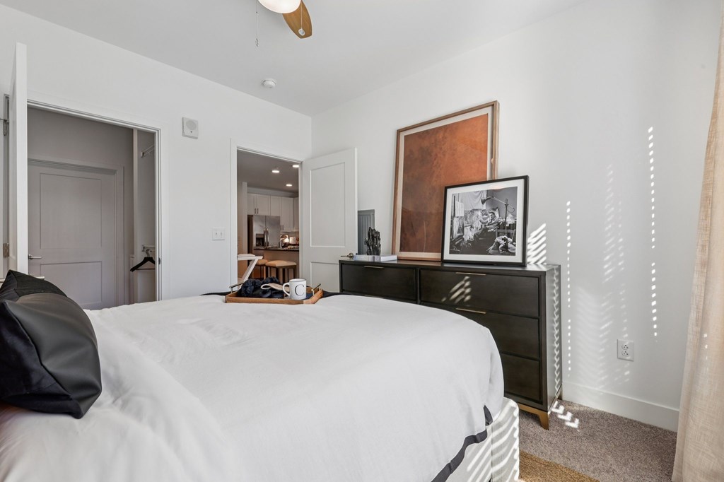 Cozy bedroom at Contrast OTR apartments in Over-the-Rhine, Cincinnati showcasing textured artwork, modern dresser, and warm sunlight.