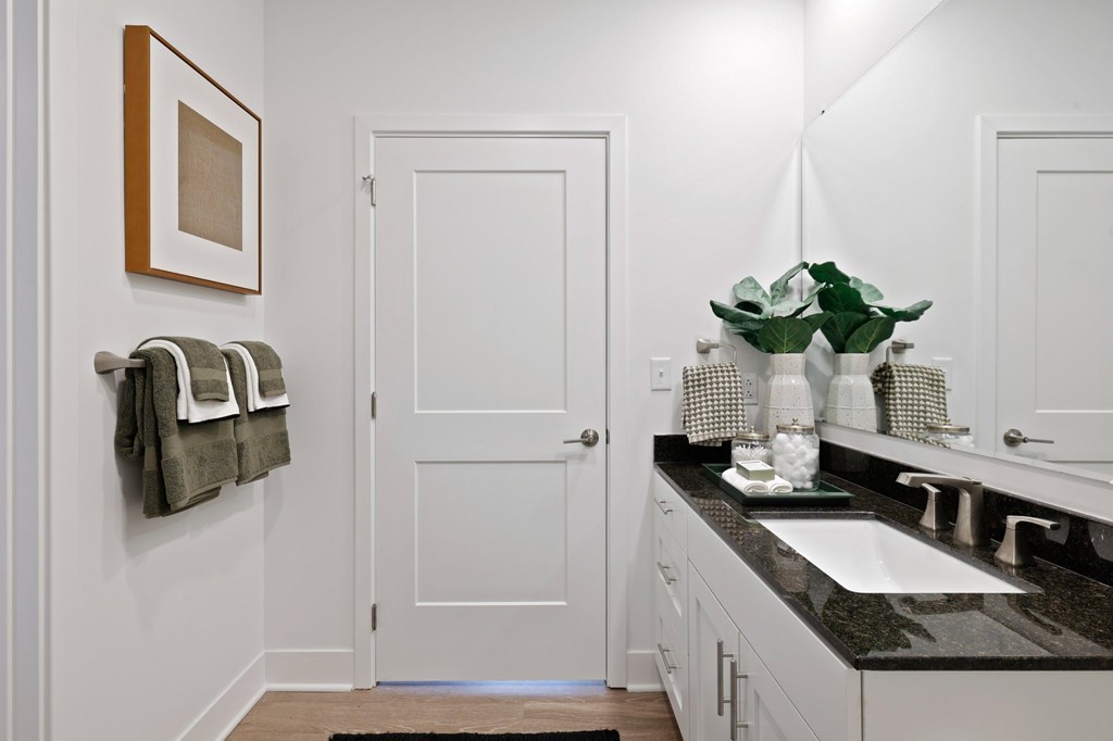 Modern bathroom at Contrast OTR in Cincinnati, OH featuring glass shower, granite countertops, and sleek white cabinetry.