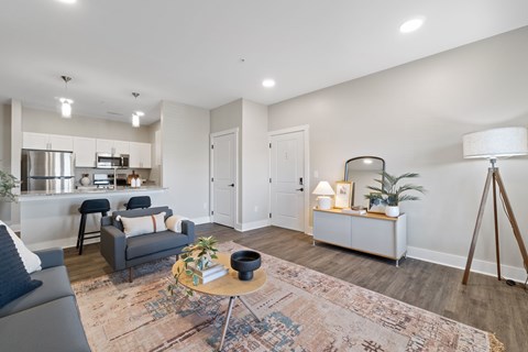 A modern living room with a grey sofa, a round table with a plant on it, and a white cabinet with a lamp on top.
