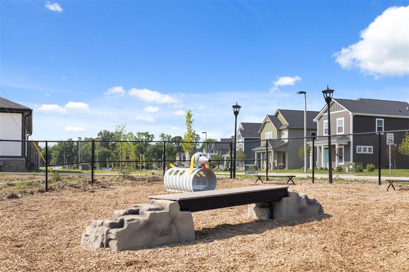 Fenced dog park with agility tunnel and bench seating at Nook Nine apartment community