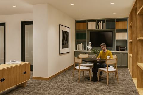 A man in a yellow shirt is sitting at a table with a laptop