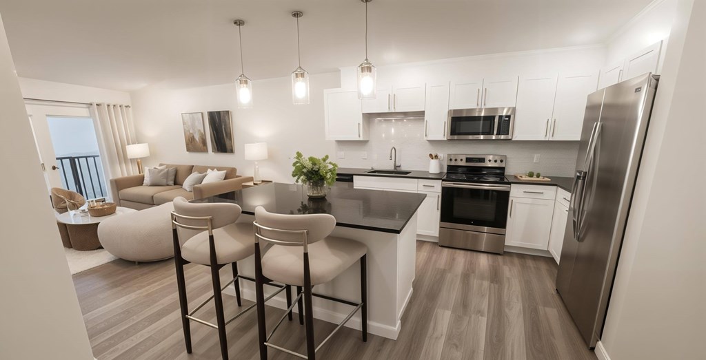 A modern kitchen with a dining area and a refrigerator. Bright and stylish kitchen at Contrast OTR in Cincinnati, Ohio, showcasing a spacious island, stainless steel appliances, white cabinetry, and modern pendant lighting