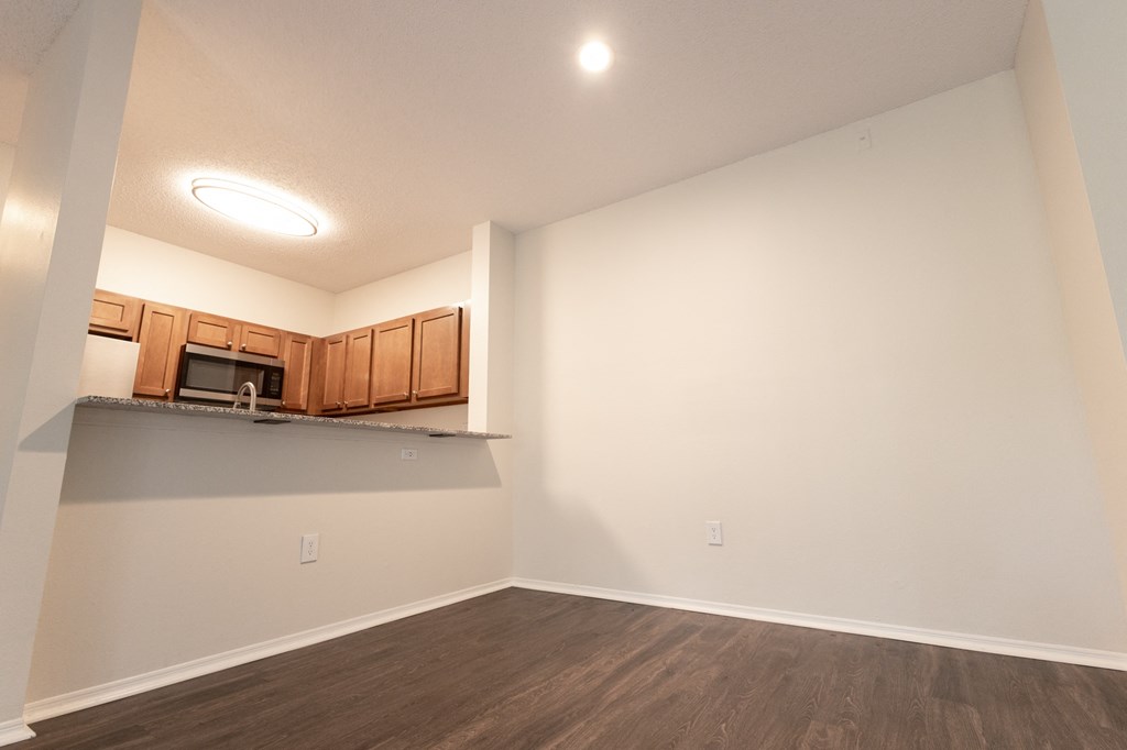 an empty living room and kitchen with wood flooring and white walls