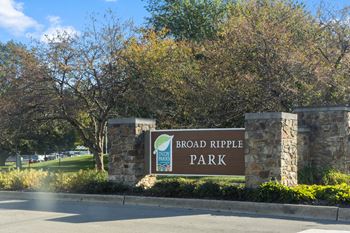 A sign for Broad Ripple Park stands in front of a tree.