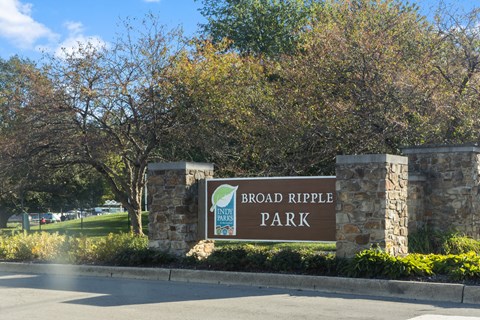 A sign for Broad Ripple Park stands in front of a tree.