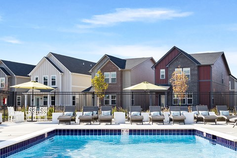 A pool area with lounge chairs and umbrellas in front of a row of houses.