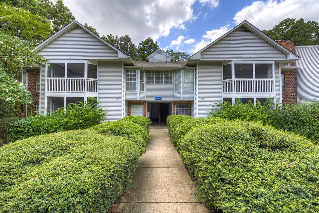 A two-story house with a driveway and hedges.
